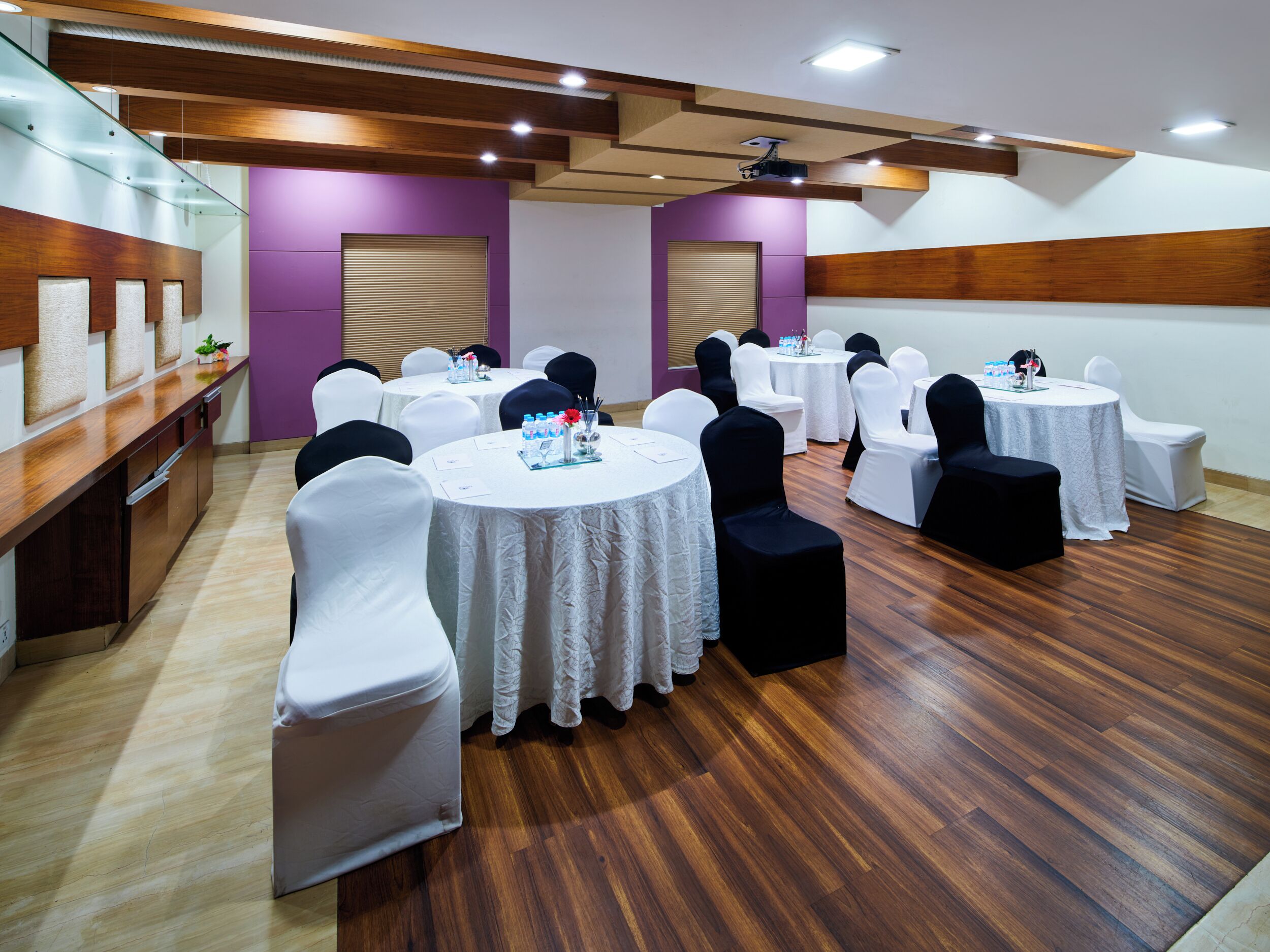A conference room with round tables, white chairs, and a wooden floor.