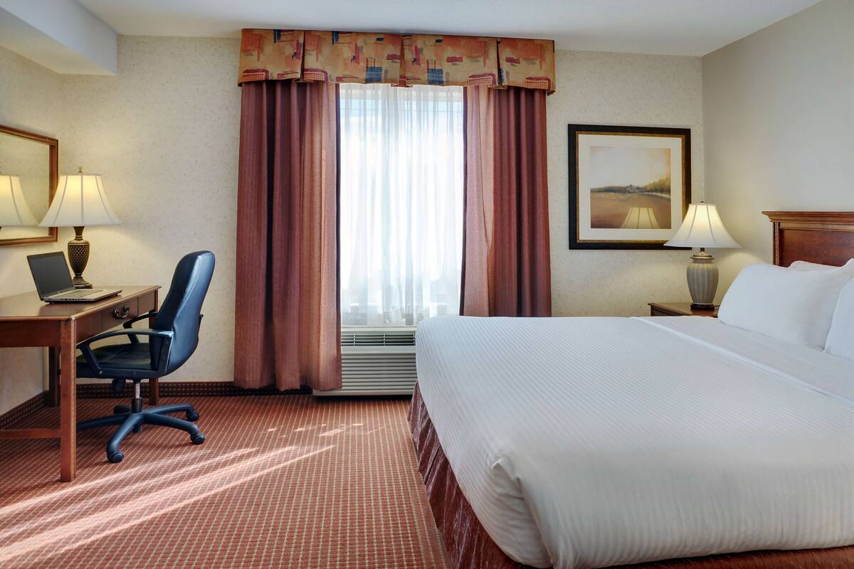 A hotel room with a bed, desk, chair, and two lamps.