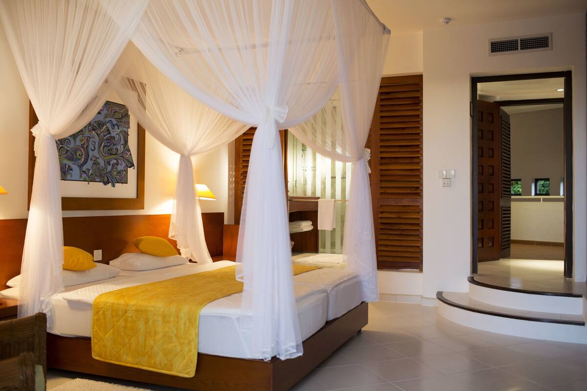 A bedroom with a four-poster bed, a bedside table, and a large mirror.
