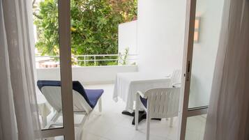 Ein Balkon mit weißen Stühlen und einem Tisch, umgeben von Grünpflanzen und einer weißen Mauer.