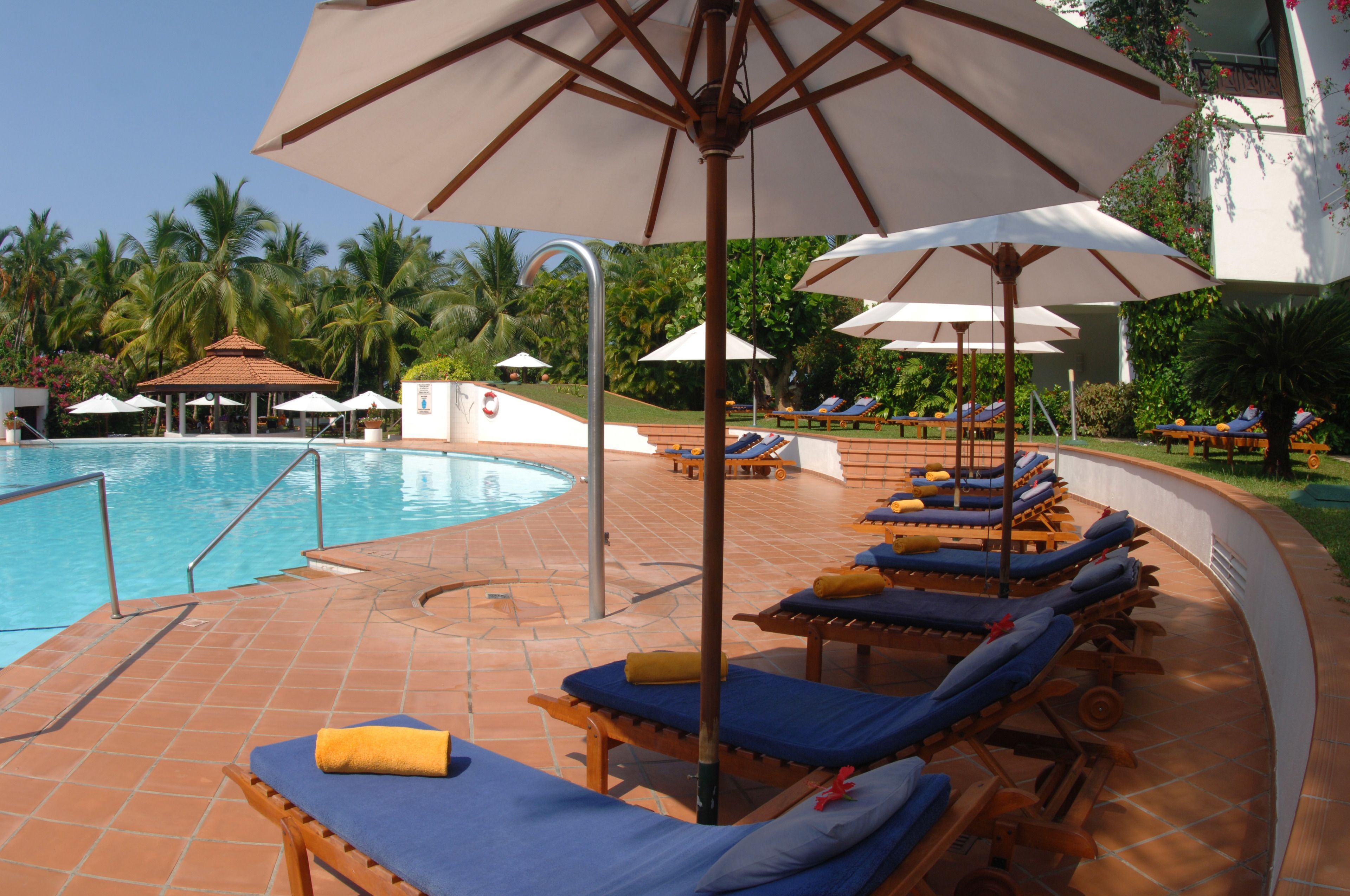 A poolside area with lounge chairs and umbrellas, surrounded by palm trees.