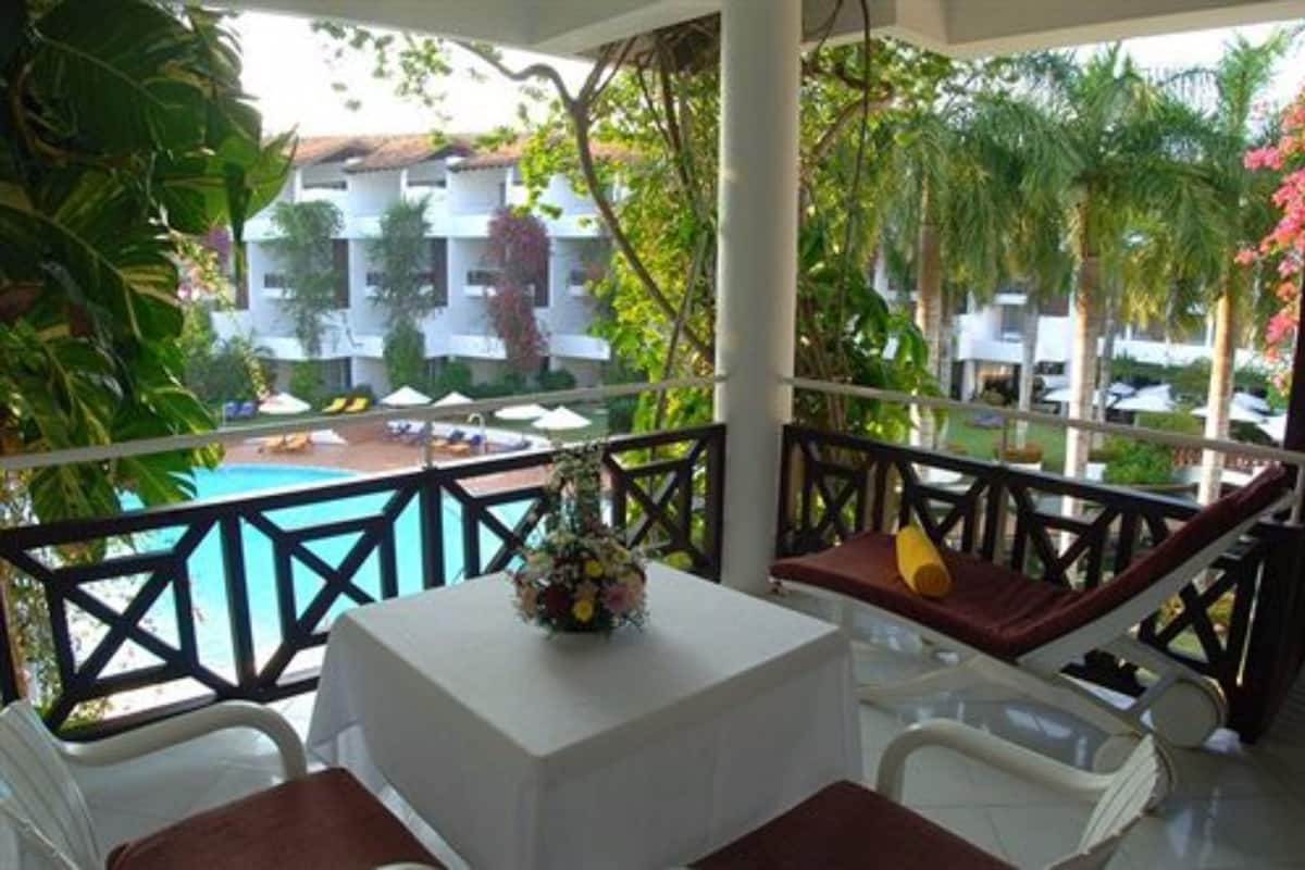 A balcony with a table and chairs, overlooking a pool and buildings.
