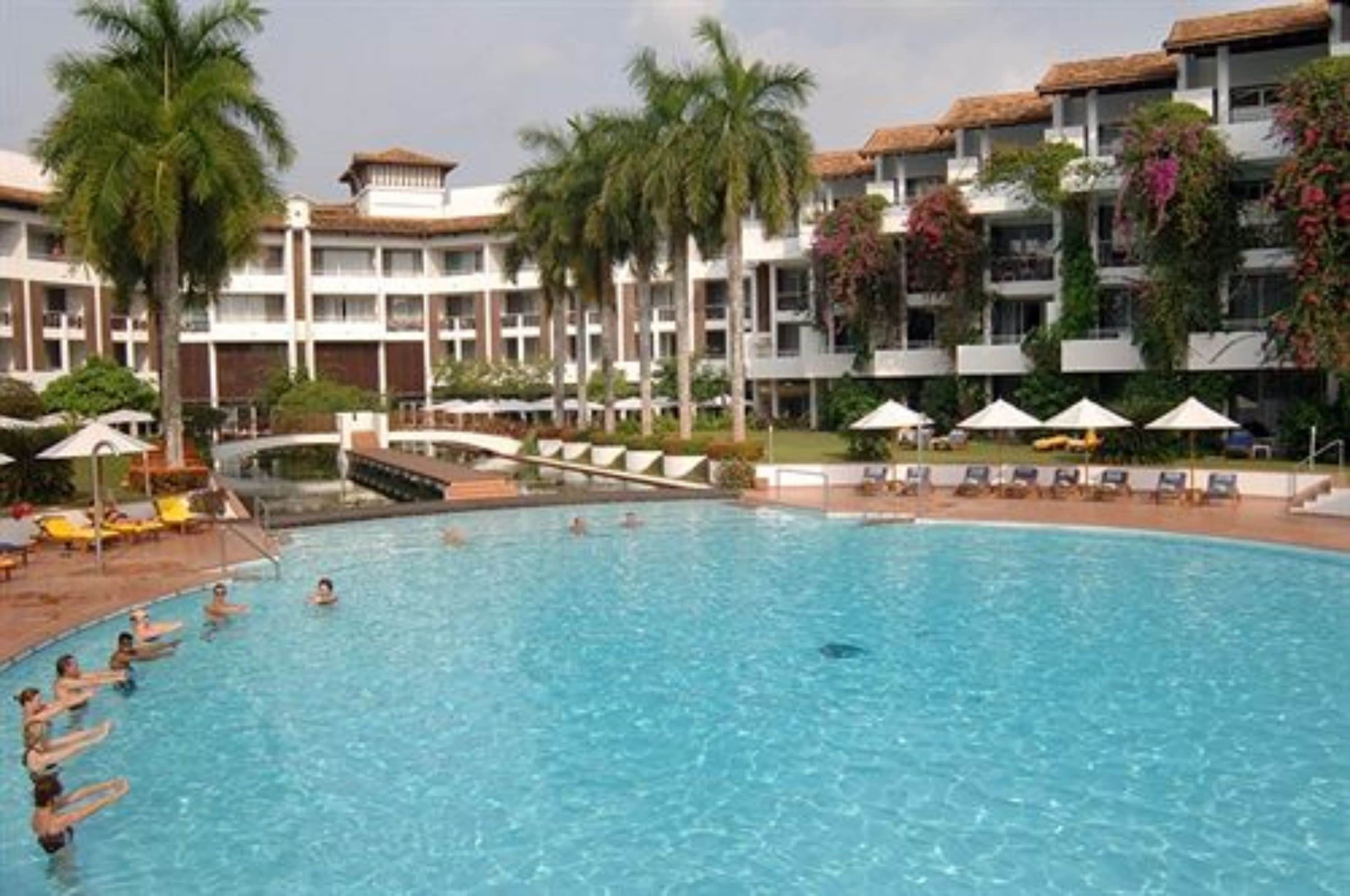 A hotel pool area with multiple levels of balconies, palm trees, and lounge chairs.
