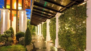 Corredor bem iluminado com piso refletivo, cercado por vegetação exuberante e pilares brancos.