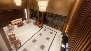 Um hall amplo com design moderno, apresentando uma área de estar com sofás e cadeiras, uma mesa central e um grande candelabro.