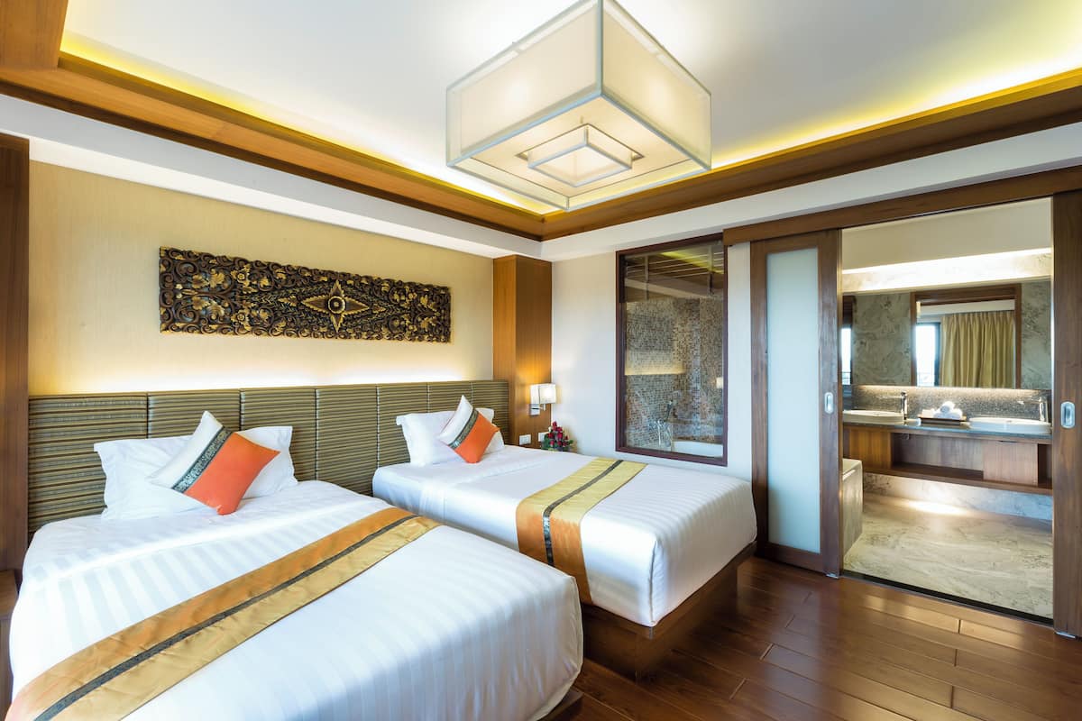 A hotel room with two beds, a large decorative wall piece, a modern chandelier, and a bathroom visible through an open door.