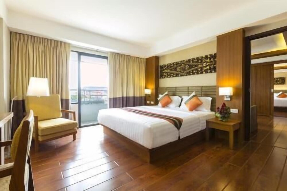 A hotel room with a large bed, a chair, a nightstand, and a view through a sliding door.
