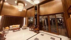 Um hall amplo com design moderno, apresentando um sofá grande, cadeiras e uma mesa de centro. Há janelas grandes e vista para o exterior.