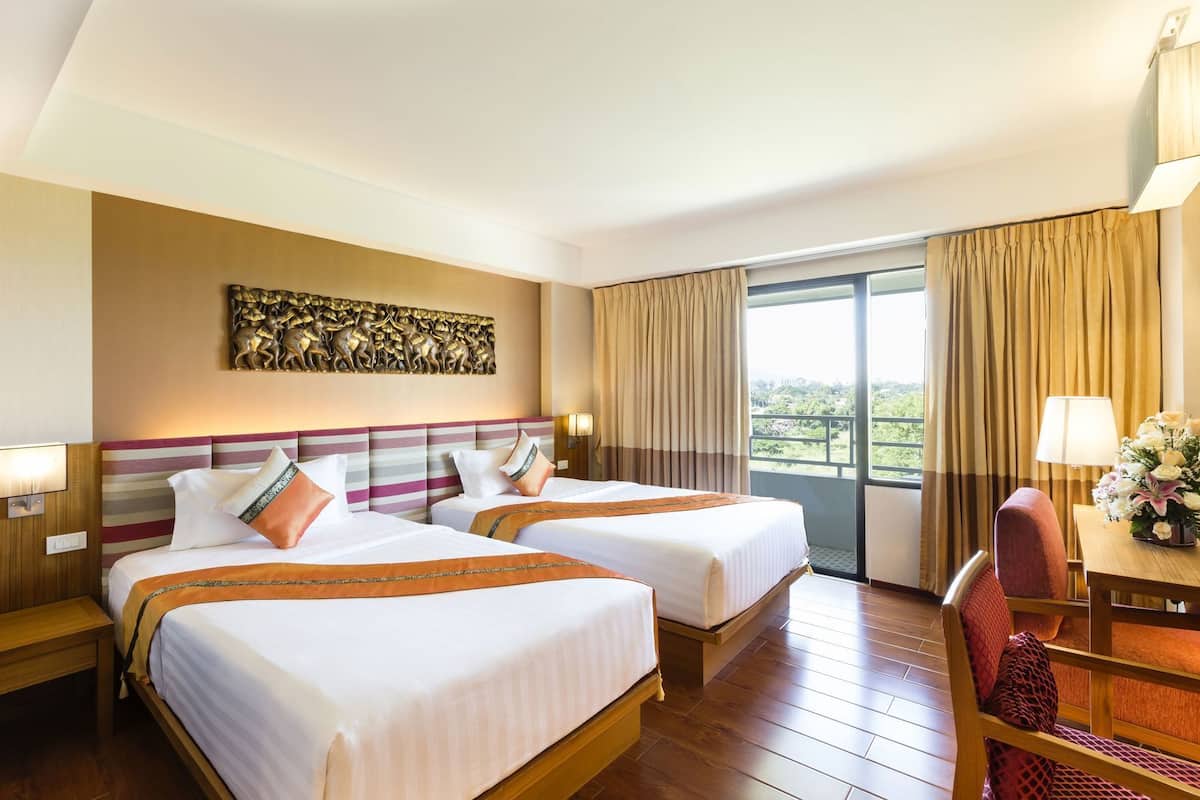 A hotel room with two beds, a desk, a chair, a large window with curtains, and a decorative wall piece.