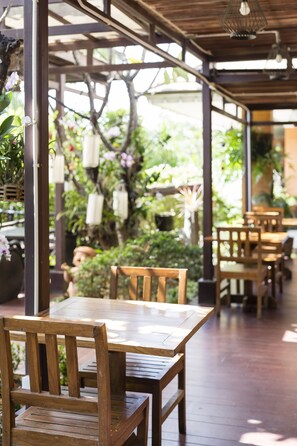 A wooden table and chairs in a covered outdoor area with hanging lanterns and greenery in the background. - Asia Hotels Group - Poonpetch Chiangmai (Chiang Mai)