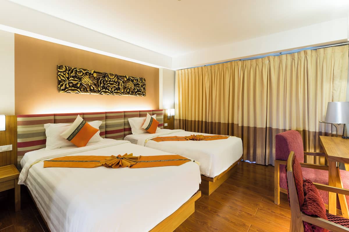 A hotel room with two beds, a wooden floor, a decorative wall piece, a curtain, a chair, and a table.