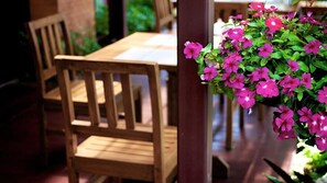 A wooden dining table with chairs, a hanging flower basket with pink flowers, and a brick wall in the background. - Asia Hotels Group - Poonpetch Chiangmai (Chiang Mai)