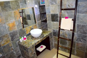 A bathroom with a stone tile backsplash, a white sink, a mirror, and a towel rack.