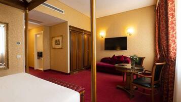 Una habitación de hotel con una cama, alfombra roja, televisión, sofá y una mesita con un jarrón.