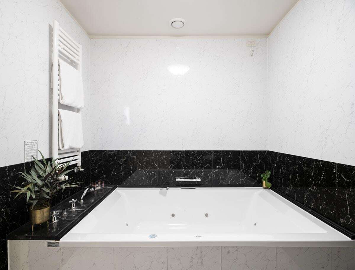 Un baño con bañera blanca, encimera de mármol negro y una planta en maceta.