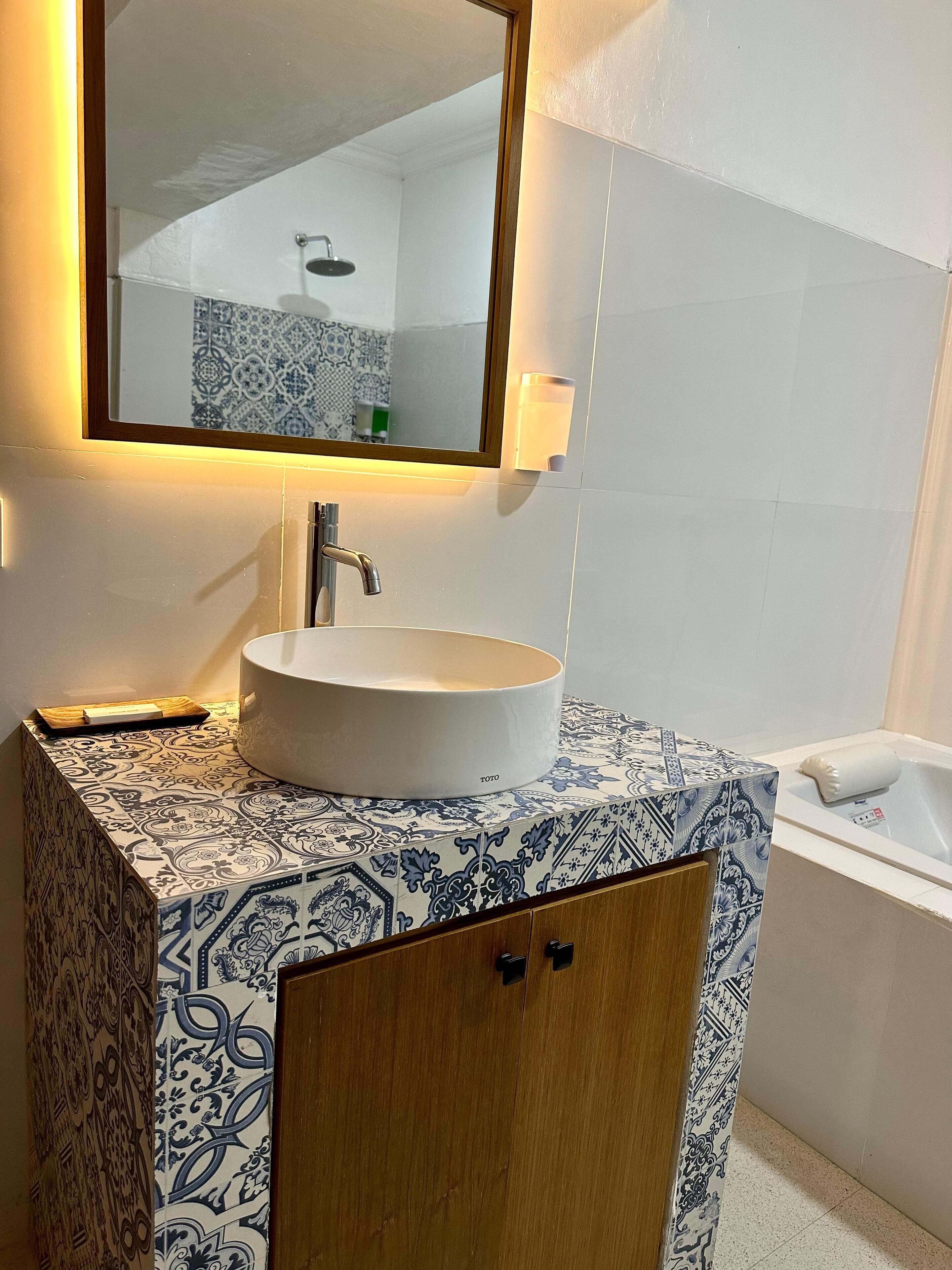 Un baño con un lavamanos blanco, un espejo y un salpicadero de azulejos con diseño.
