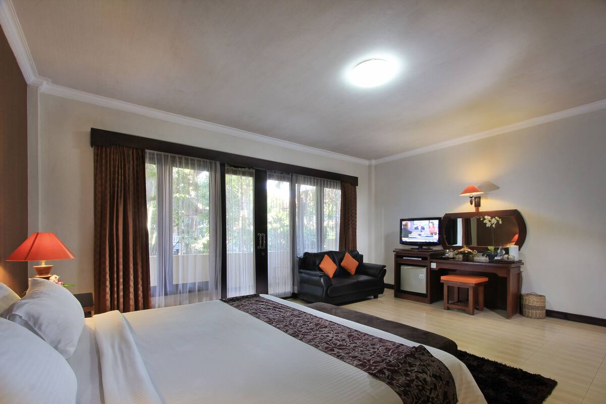 A hotel room with a large bed, a desk with a computer, a television, and a seating area with a sofa and chairs.