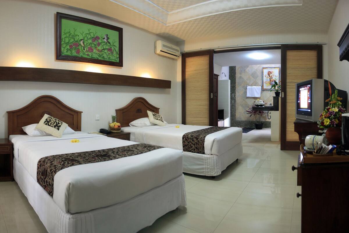 A hotel room with two beds, a television, a bathroom with a shower, and a painting on the wall.