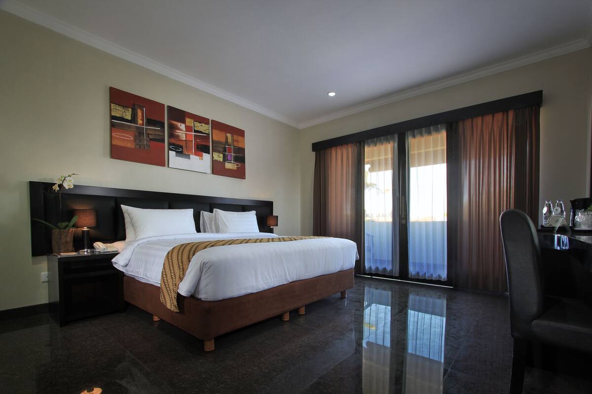 A hotel room with a large bed, a nightstand, a desk, and a chair.