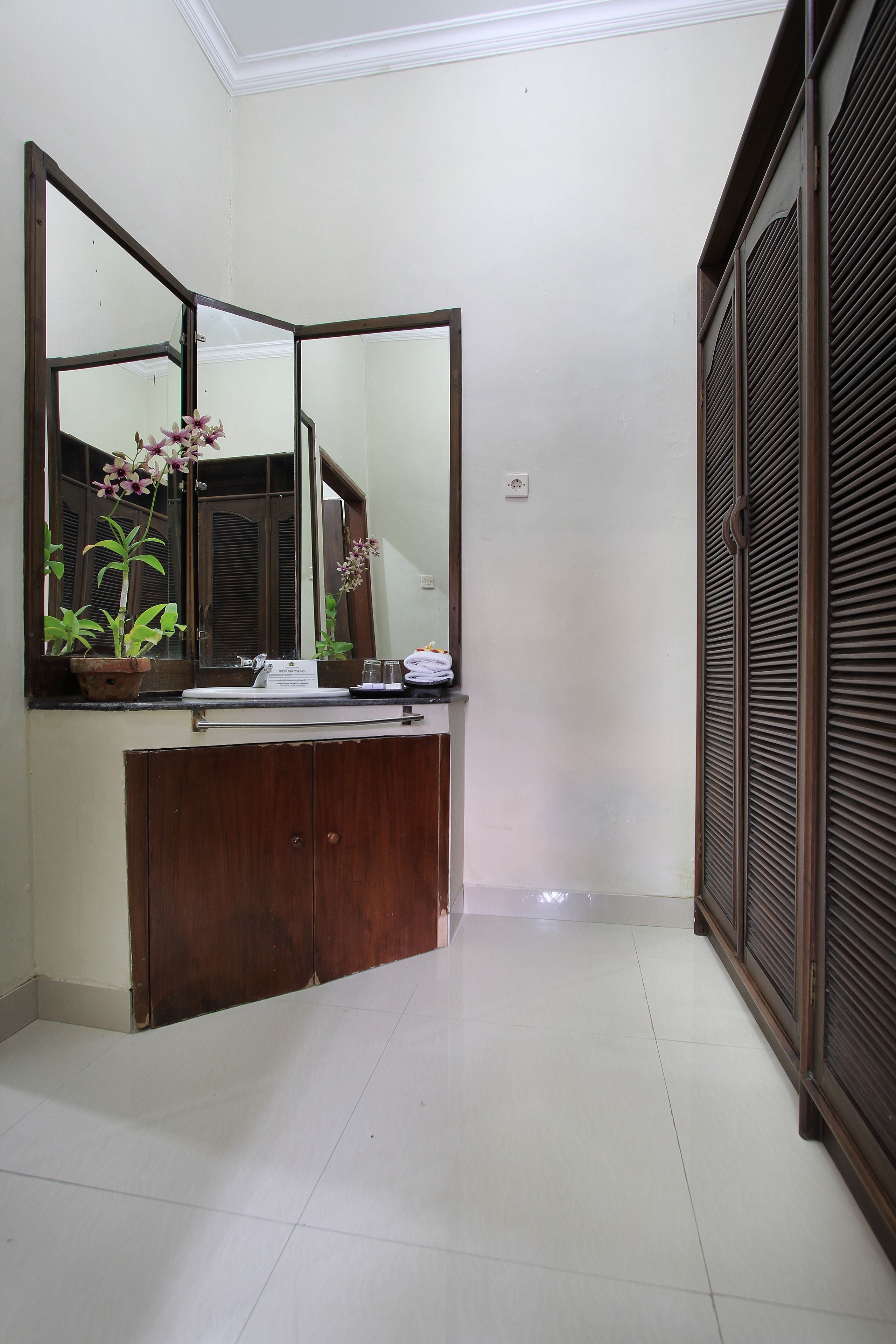 A bathroom with a wooden vanity, a large mirror, and a potted plant.