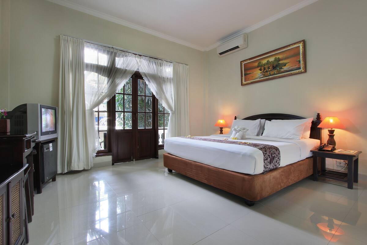 A hotel room with a large bed, two bedside lamps, a TV, and a painting on the wall.