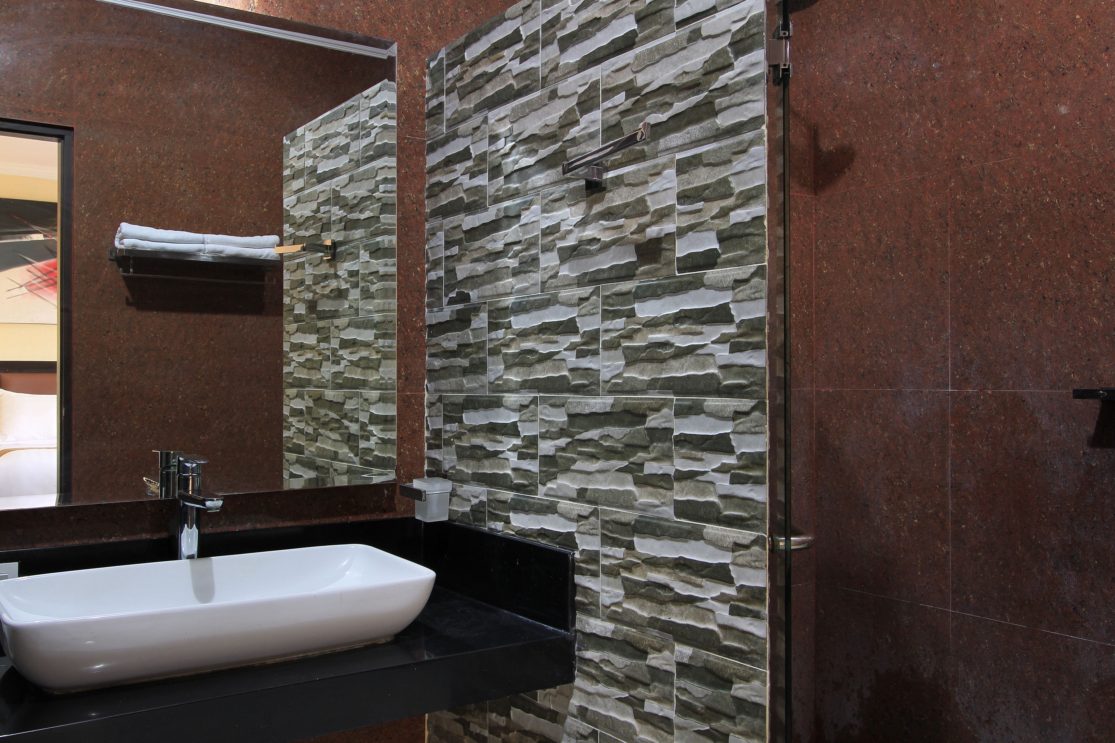 Un baño con un lavamanos rectangular, un espejo y una pared con diseño de piedra texturizada.