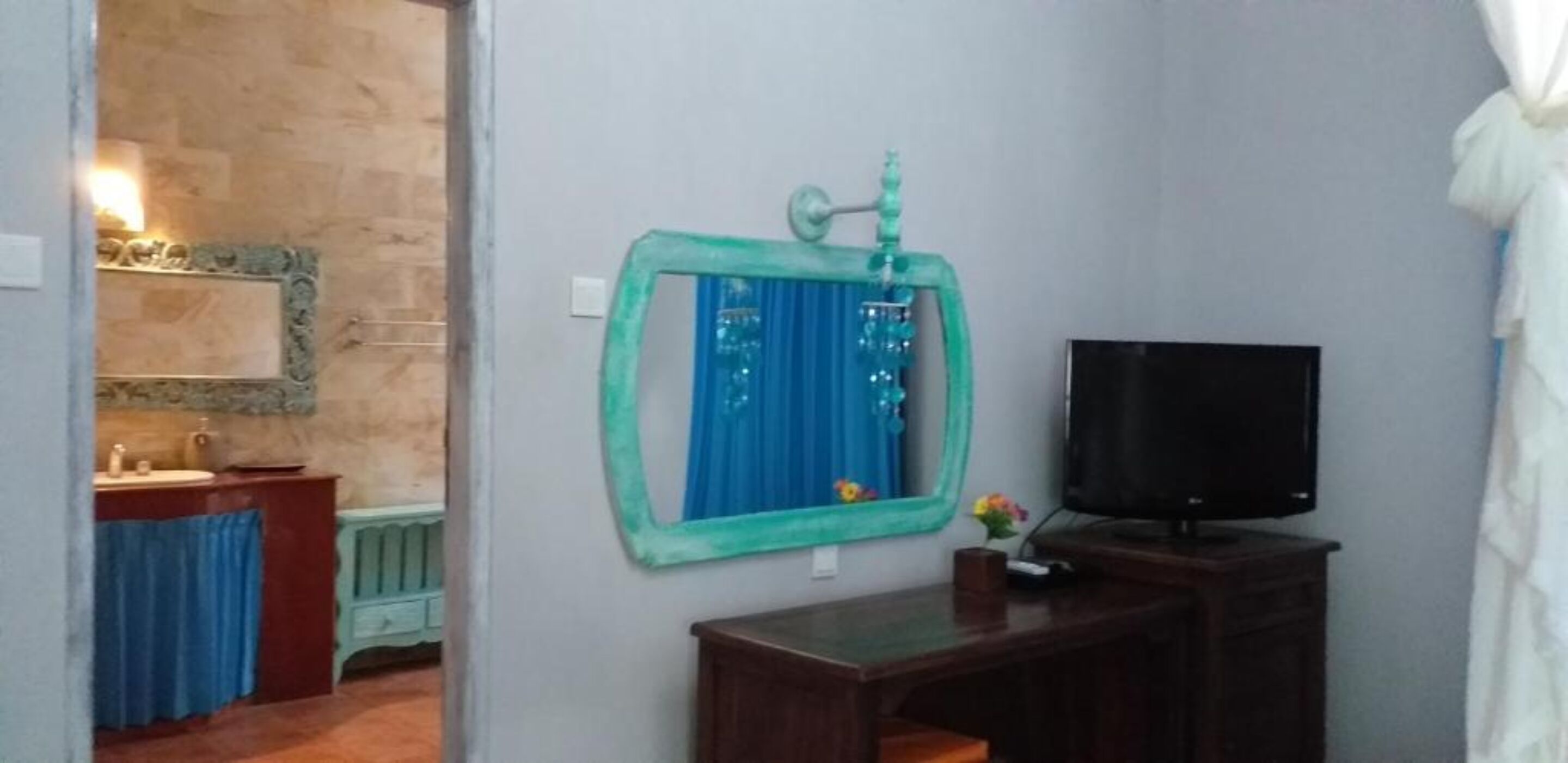 A bathroom with a mirror, a sink, a toilet, a television, and a decorative wall piece.