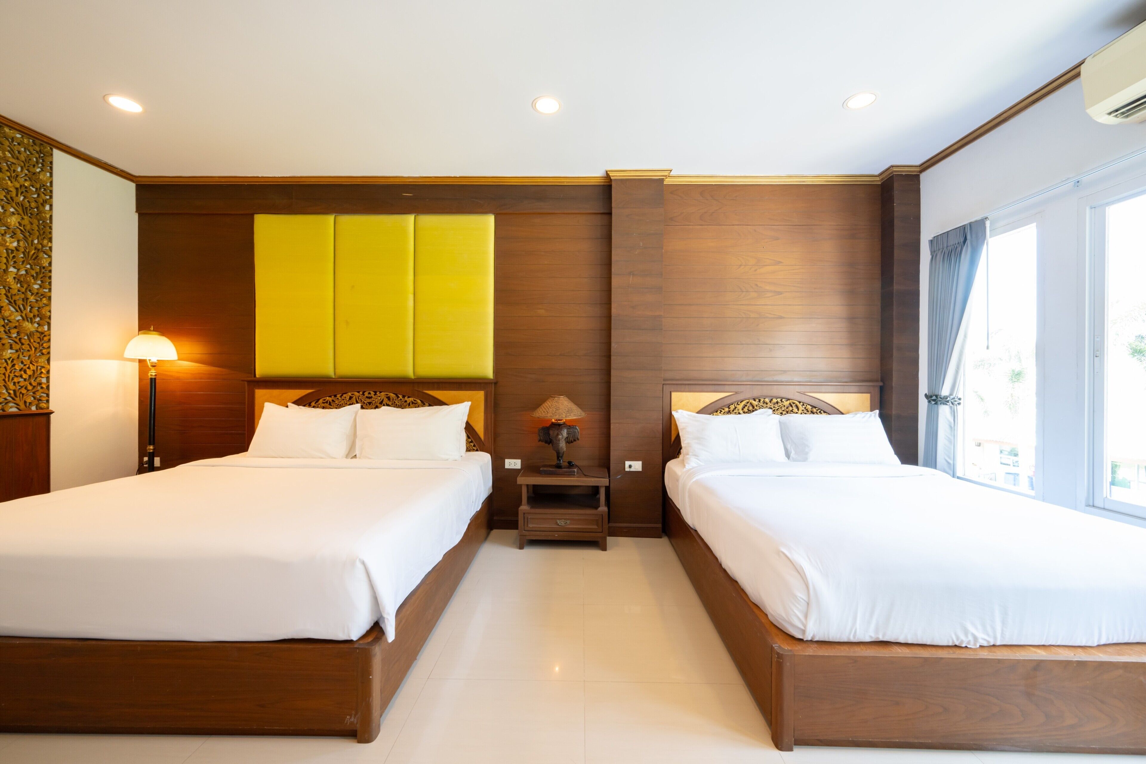 A hotel room with two beds, a nightstand with a lamp, and a window with curtains.