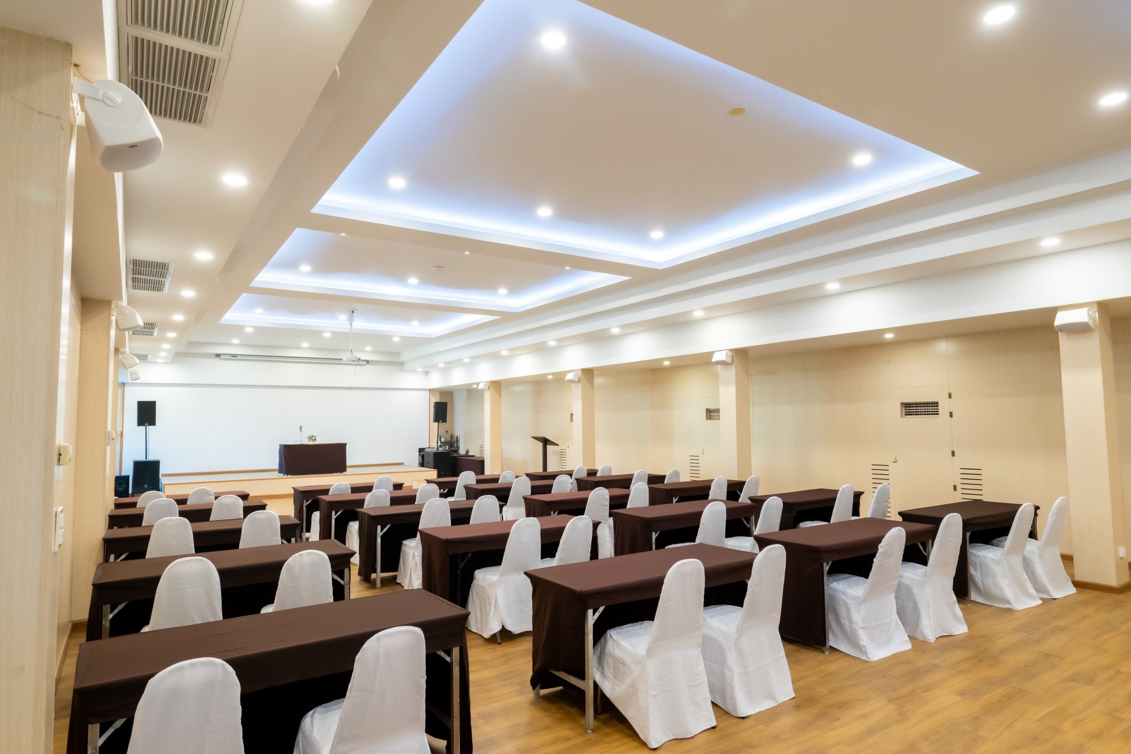 Un salón de conferencias con mesas, sillas, un atril y una pantalla para presentaciones.