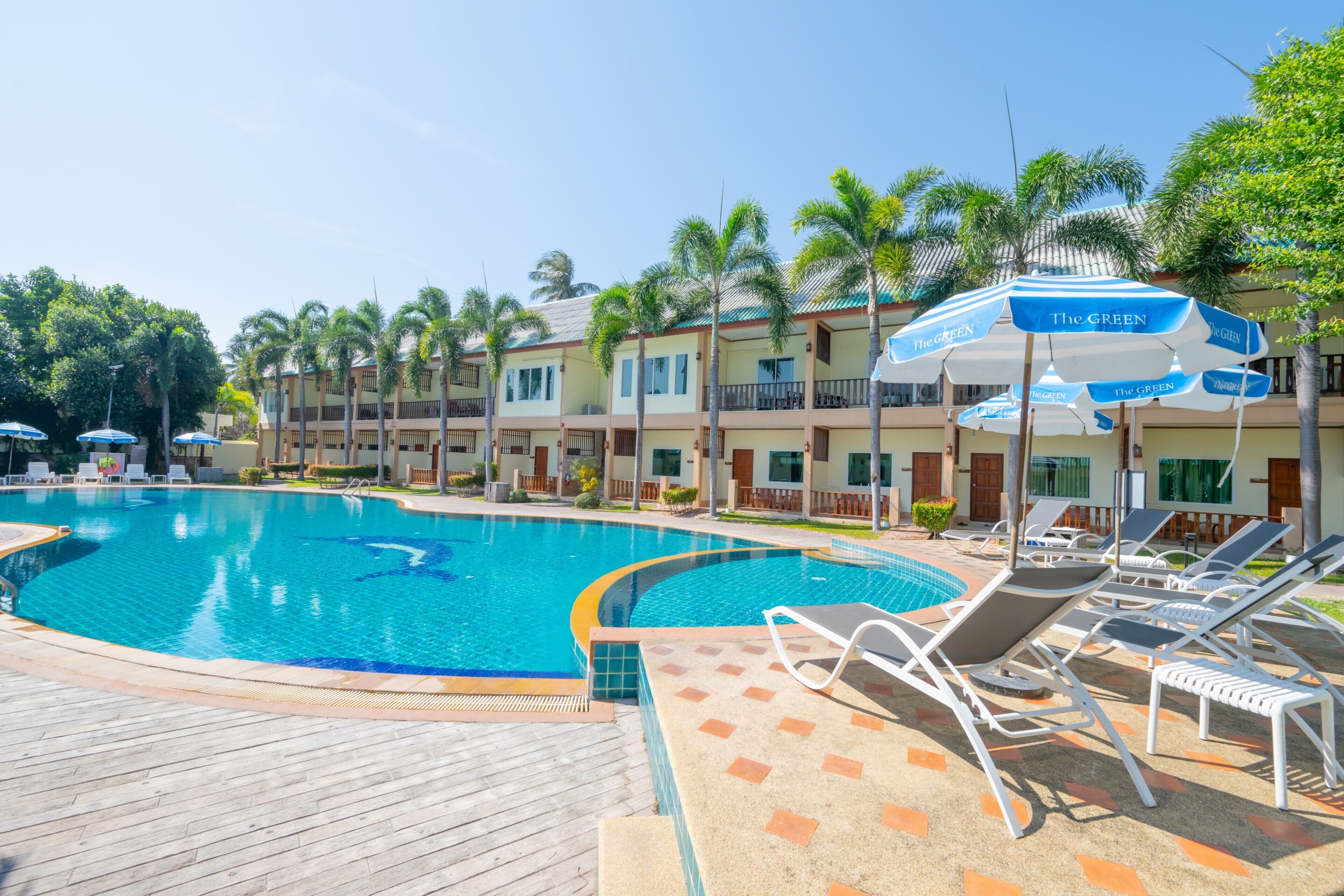 A swimming pool with lounge chairs and umbrellas, surrounded by palm trees and hotel buildings.