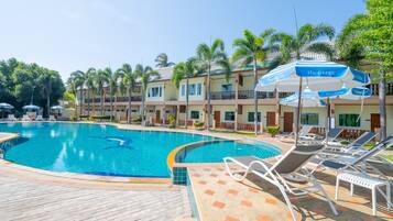 A swimming pool with lounge chairs and umbrellas, surrounded by palm trees and hotel buildings.