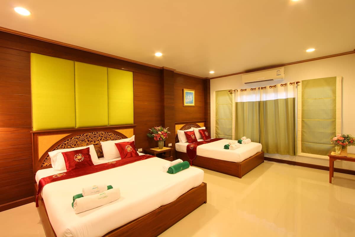 A hotel room with two beds, a wooden headboard, a window with curtains, a nightstand with a vase of flowers, and an air conditioning unit.