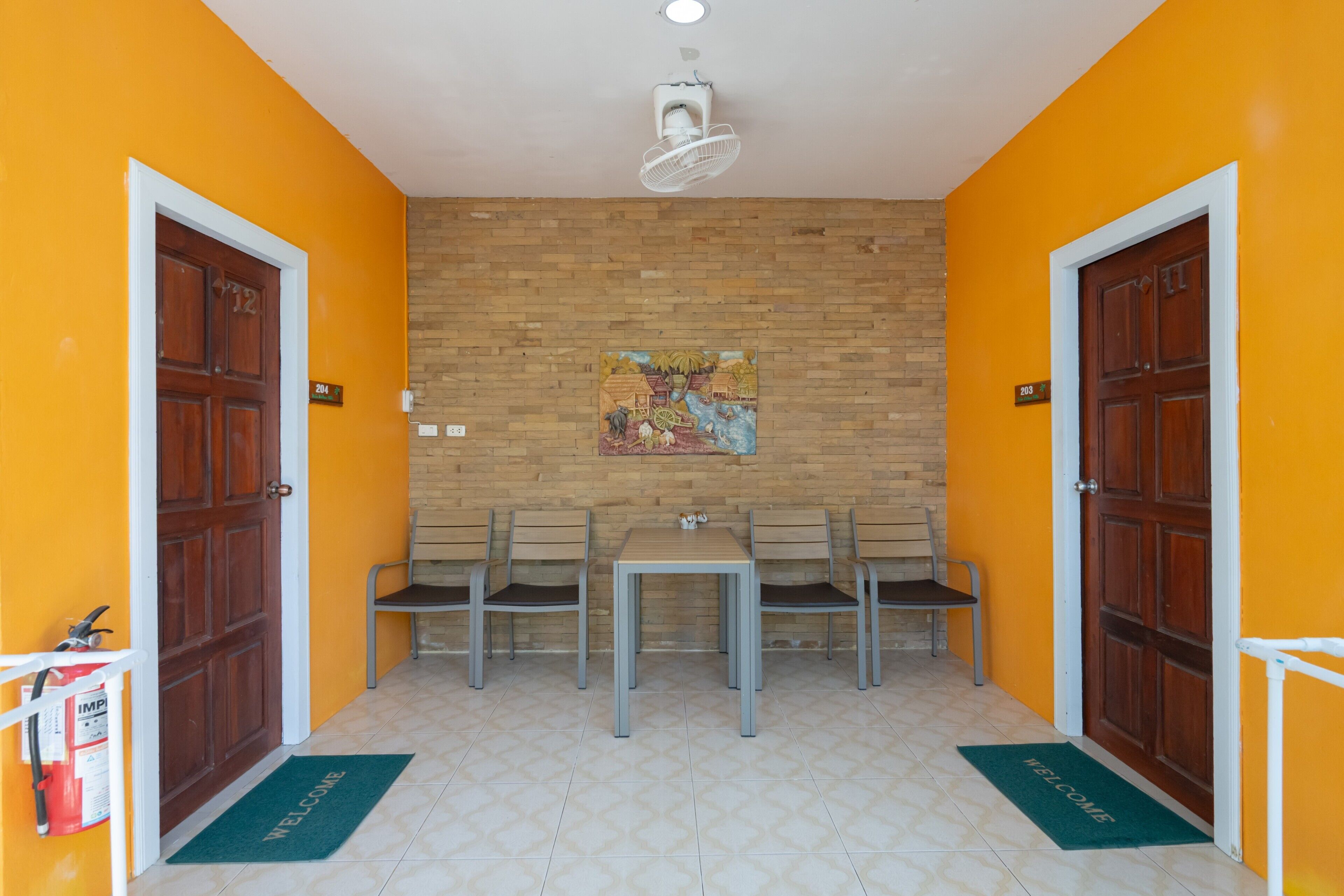 A room with a wooden door, a brick wall, a table with chairs, and a welcome mat.