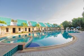 Una piscina con solárium de baldosas, sillas de descanso y una hilera de edificios con tejados verdes.