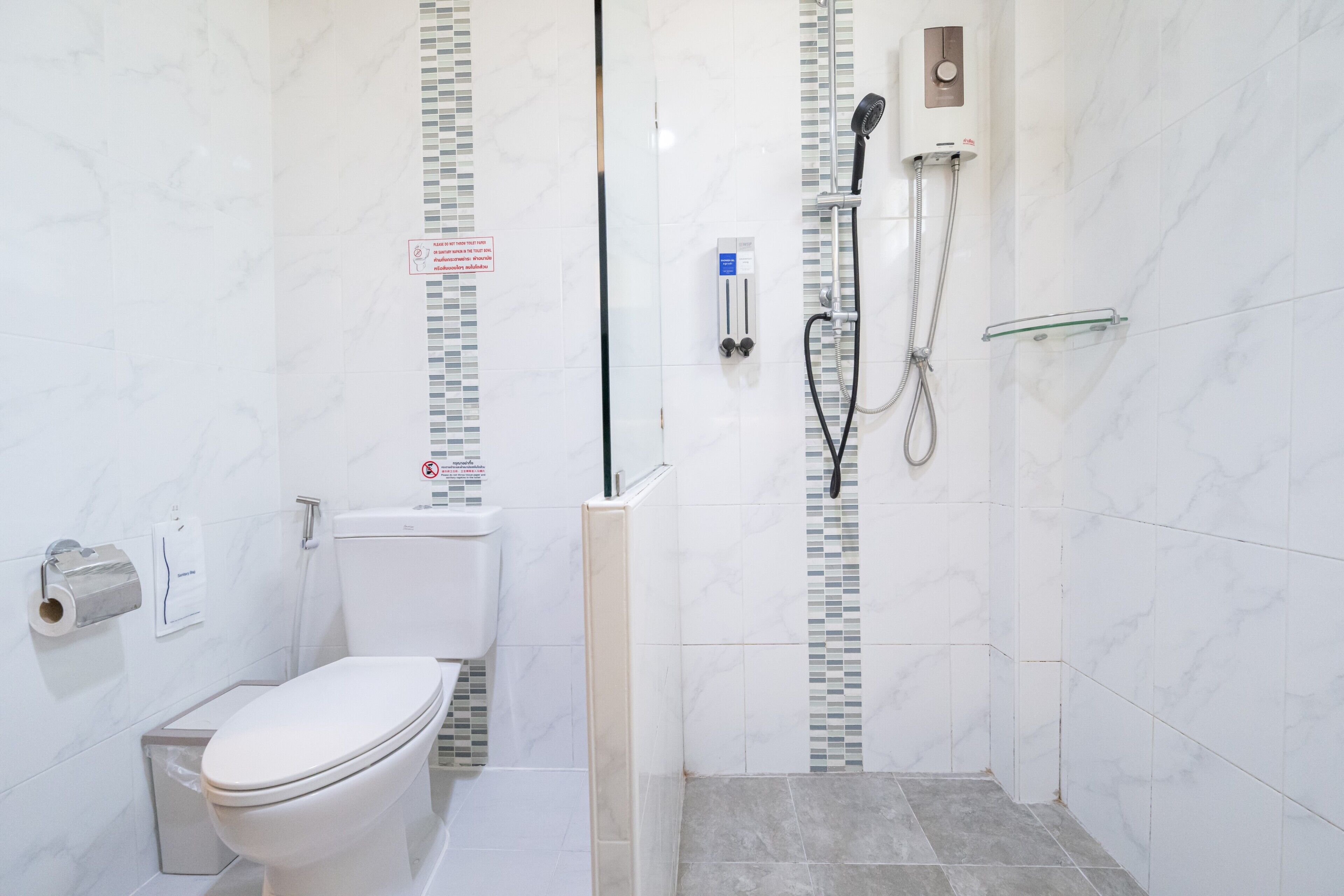 Une salle de bain comprenant des toilettes, une douche avec un pommeau de douche amovible et une étagère en verre.