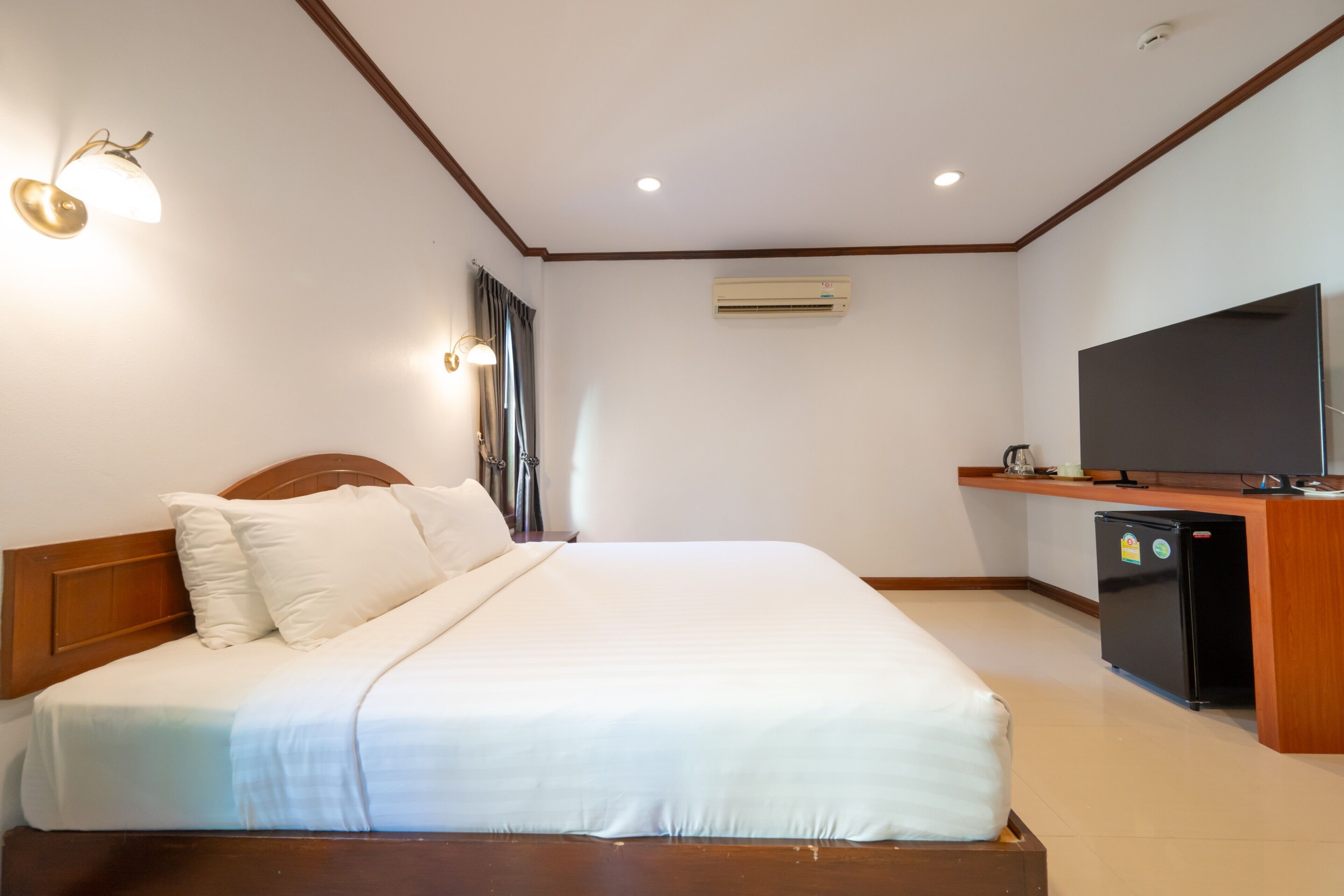 A hotel room with a bed, a television, a refrigerator, and an air conditioning unit.