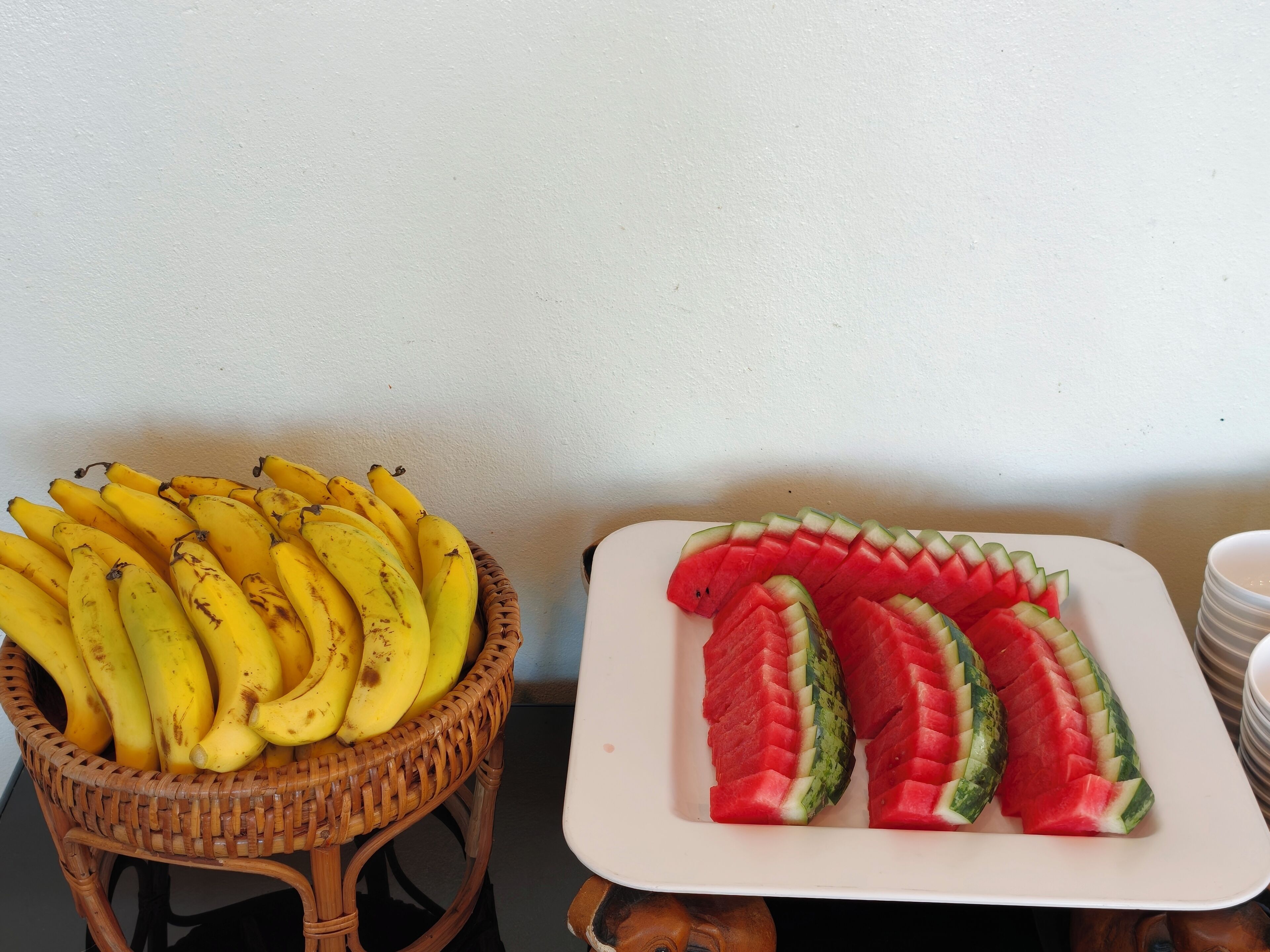 A wicker basket filled with bananas and a white plate with watermelon slices.