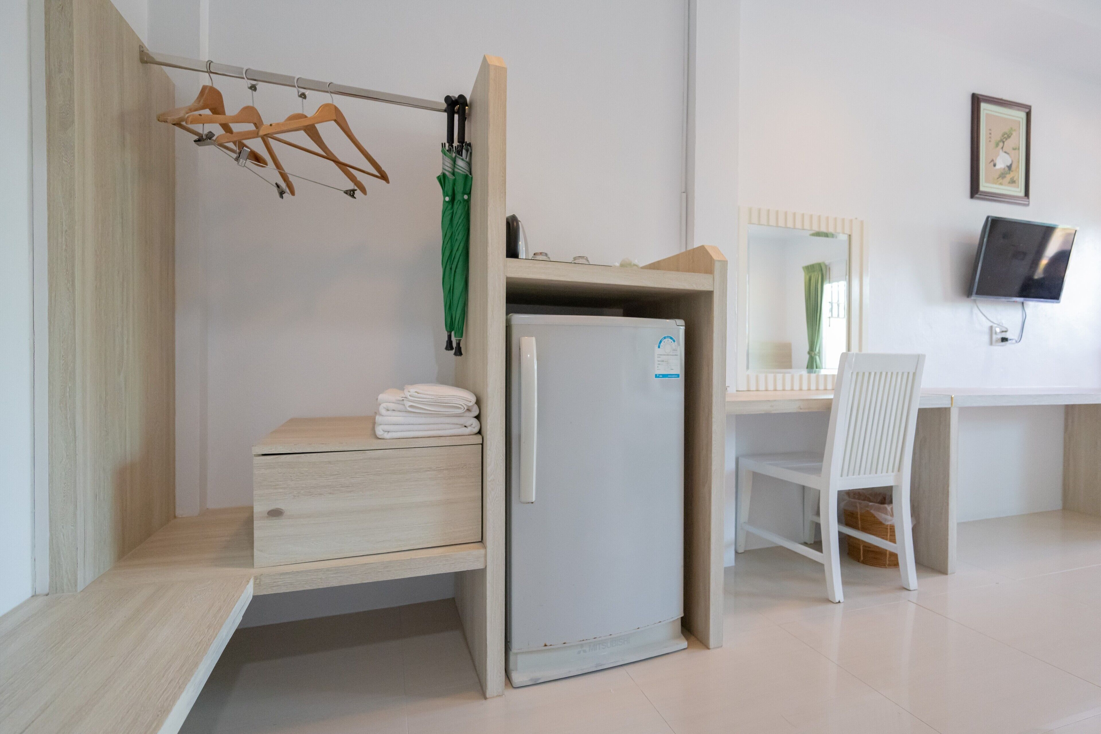 A compact hotel room with a wooden desk, a small refrigerator, a chair, and a mirror.