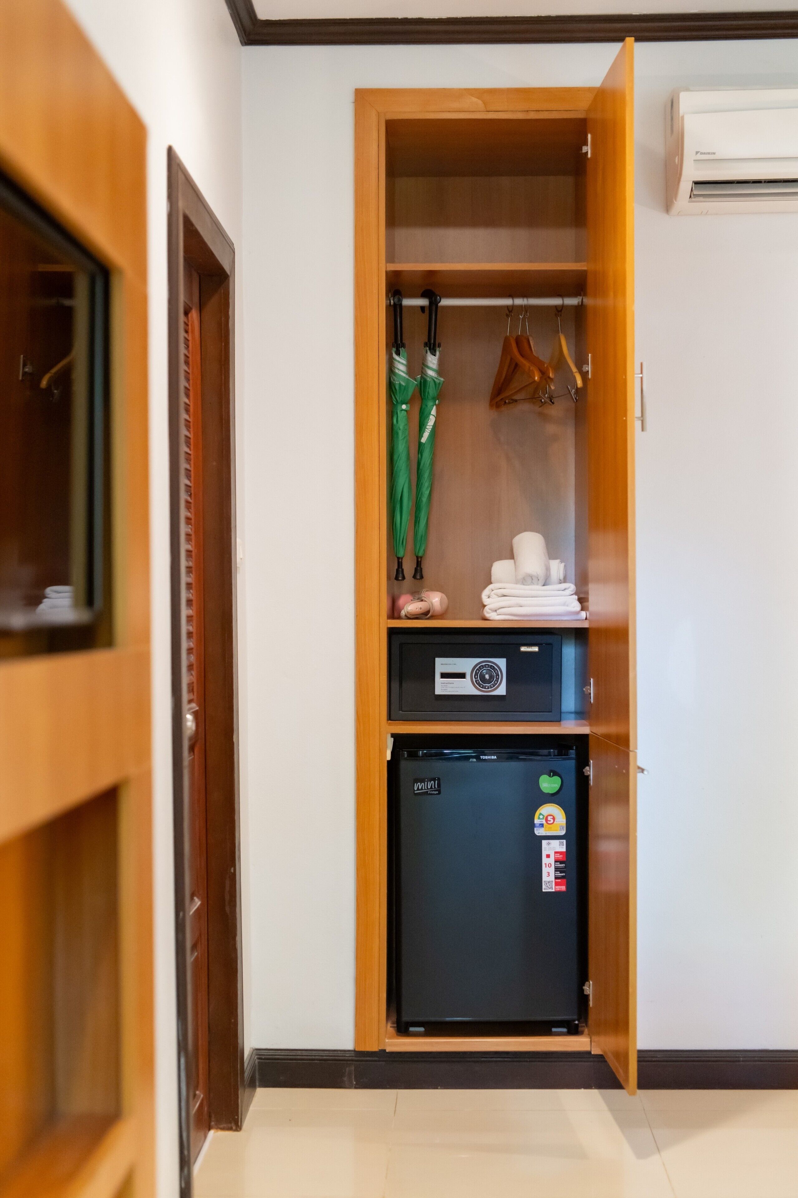 A compact room with a wooden wardrobe, a mini fridge, and a hanging rack with umbrellas.