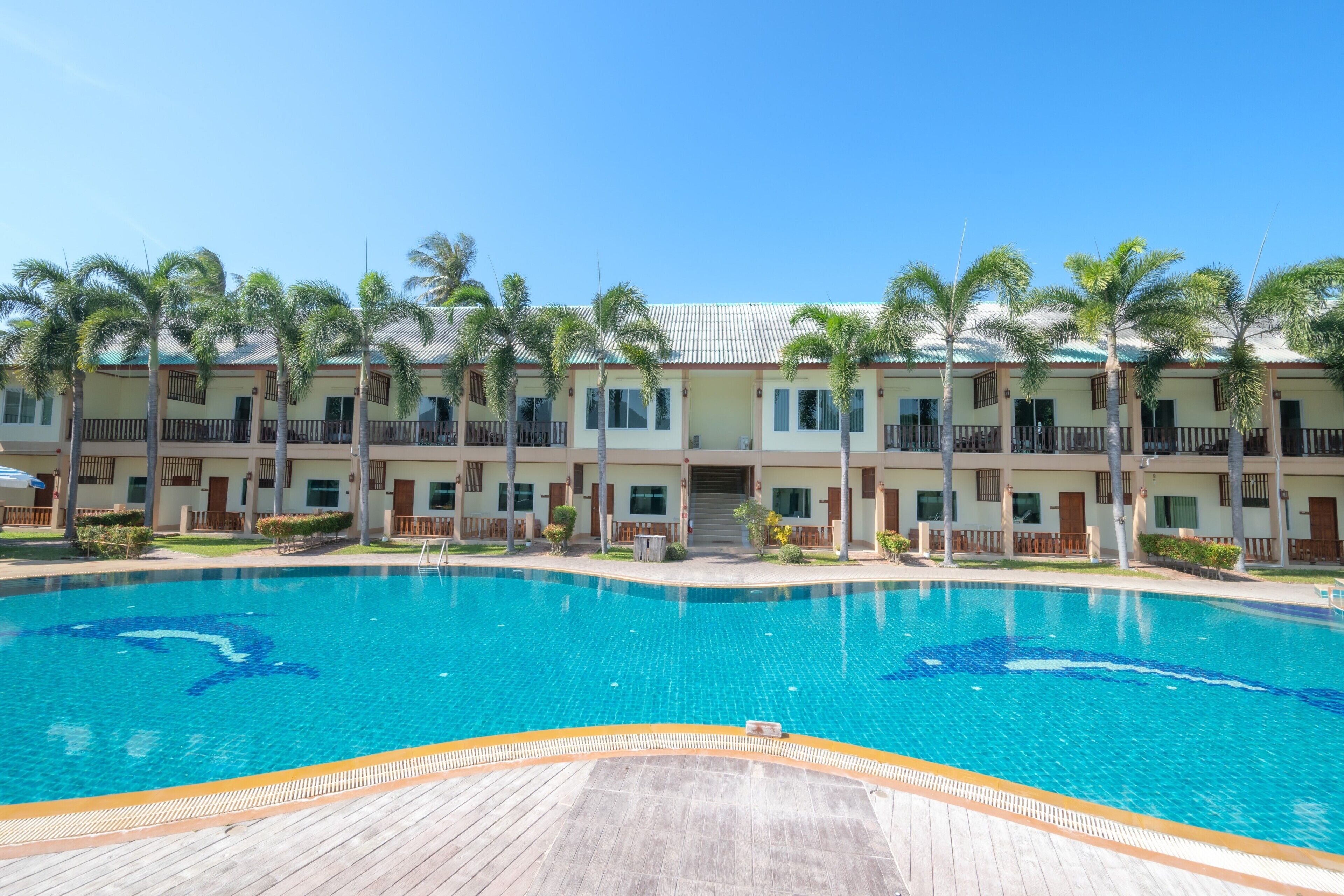 A hotel with a swimming pool, palm trees, and a wooden deck.