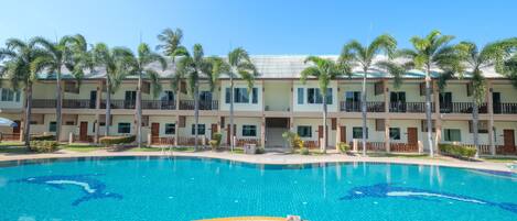 A hotel with a swimming pool, palm trees, and a wooden deck.