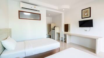 A hotel room with a bed, a desk, a chair, a television, and an air conditioning unit.