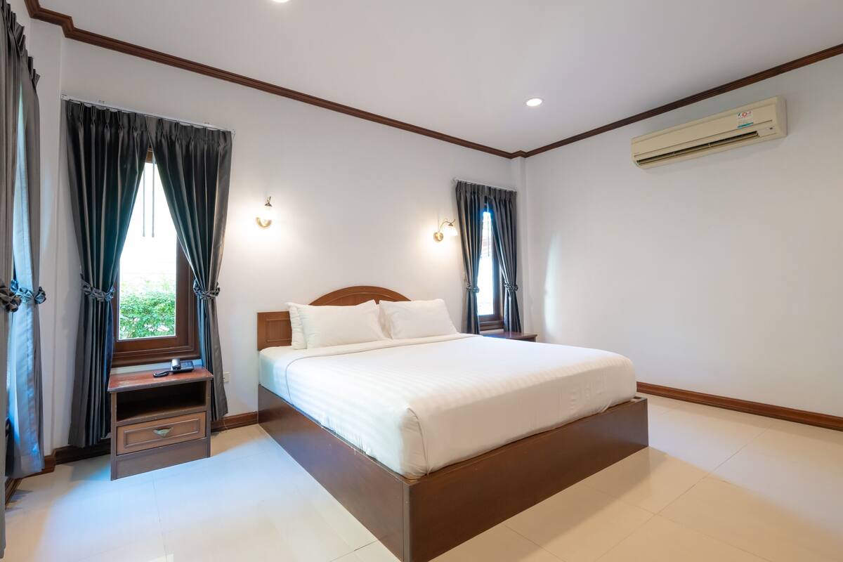 A bedroom with a wooden bed, a nightstand, a desk, and a window with curtains.