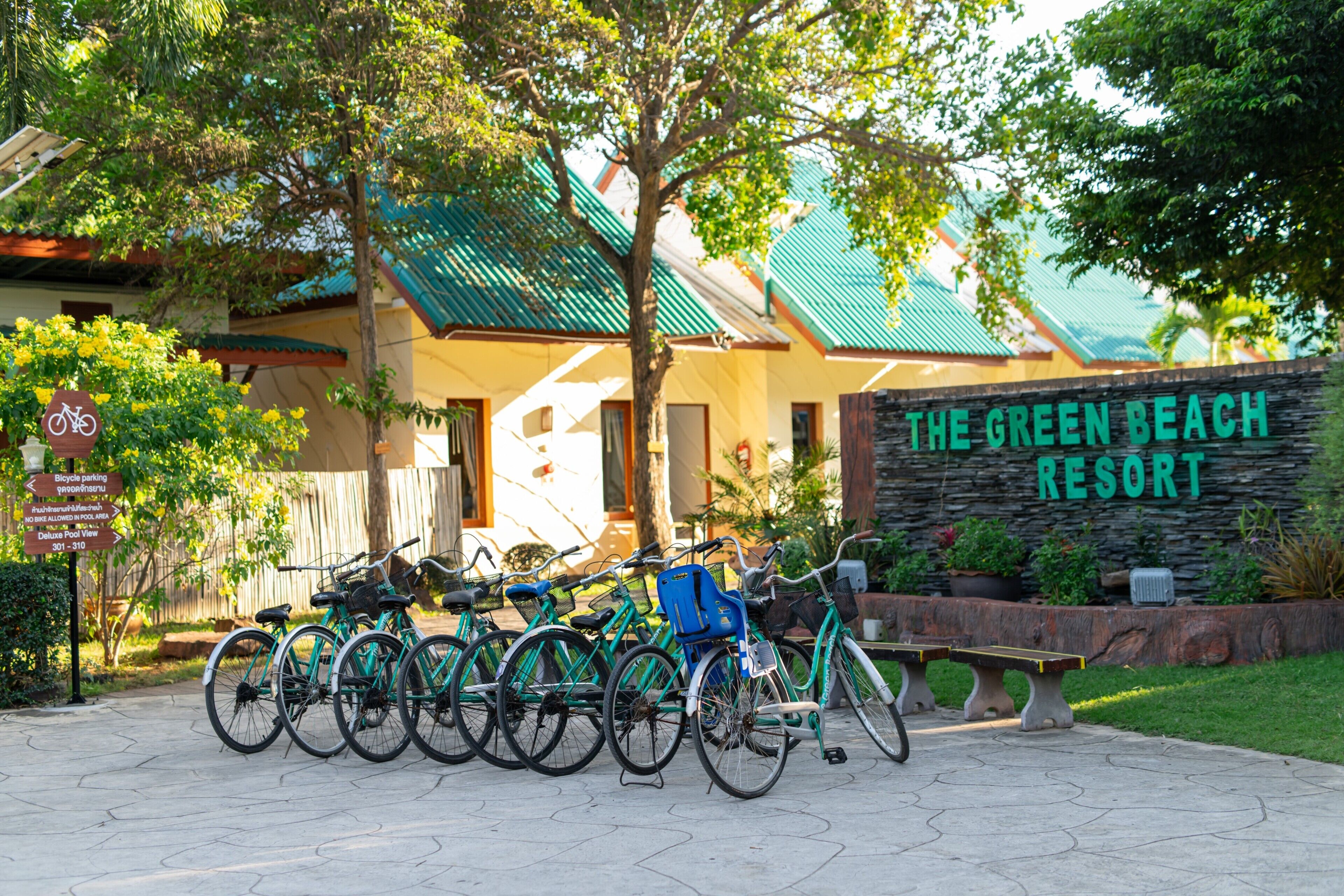 Une enseigne indiquant « The Green Beach Resort », des vélos garés devant, et un banc.