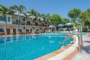 Una piscina con agua azul cristalina, rodeada de palmeras y un edificio con balcones.