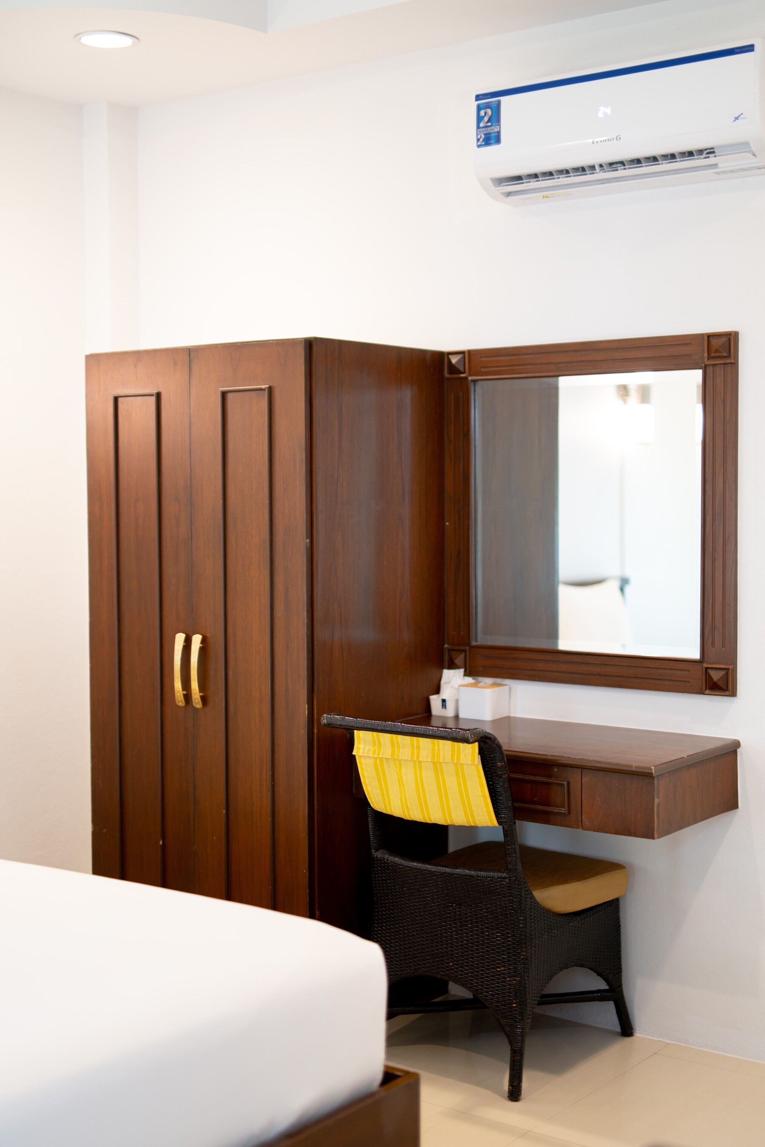A bedroom with a wooden wardrobe, a desk with a mirror, and a bed.