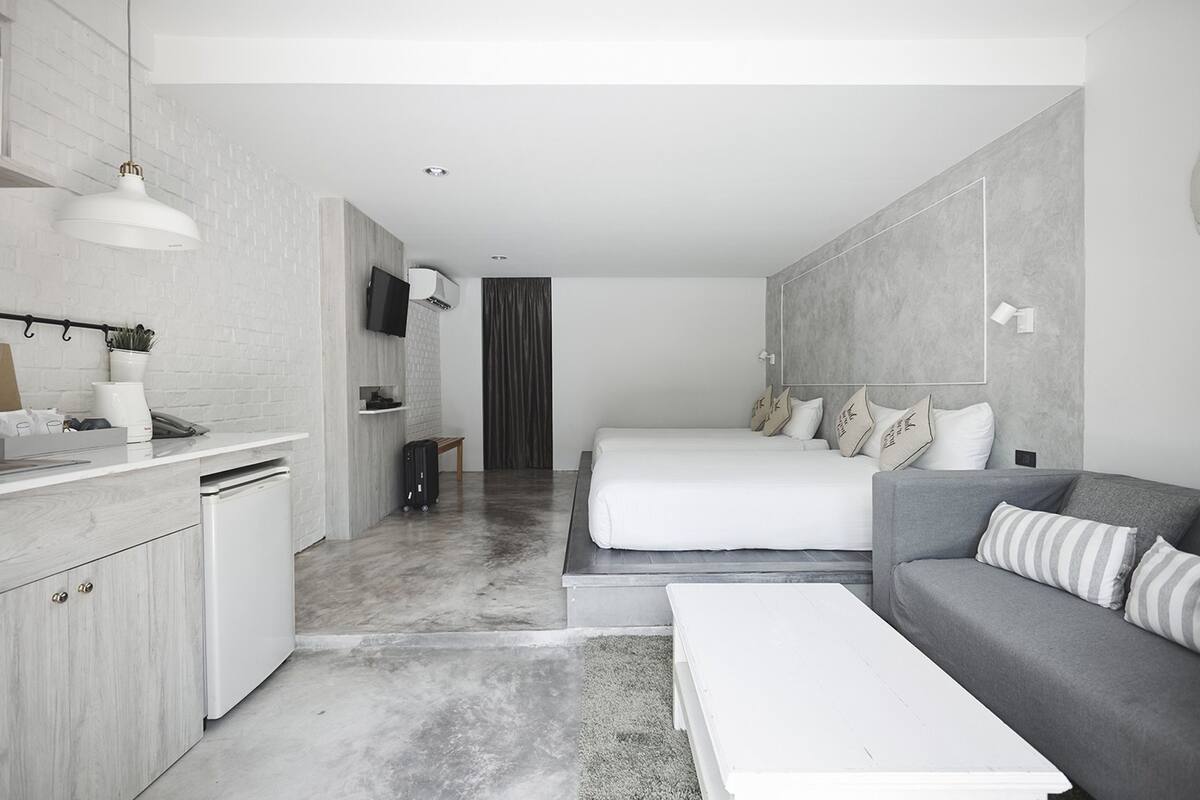 A modern hotel room with a kitchenette, a bed, a sofa, and a TV.