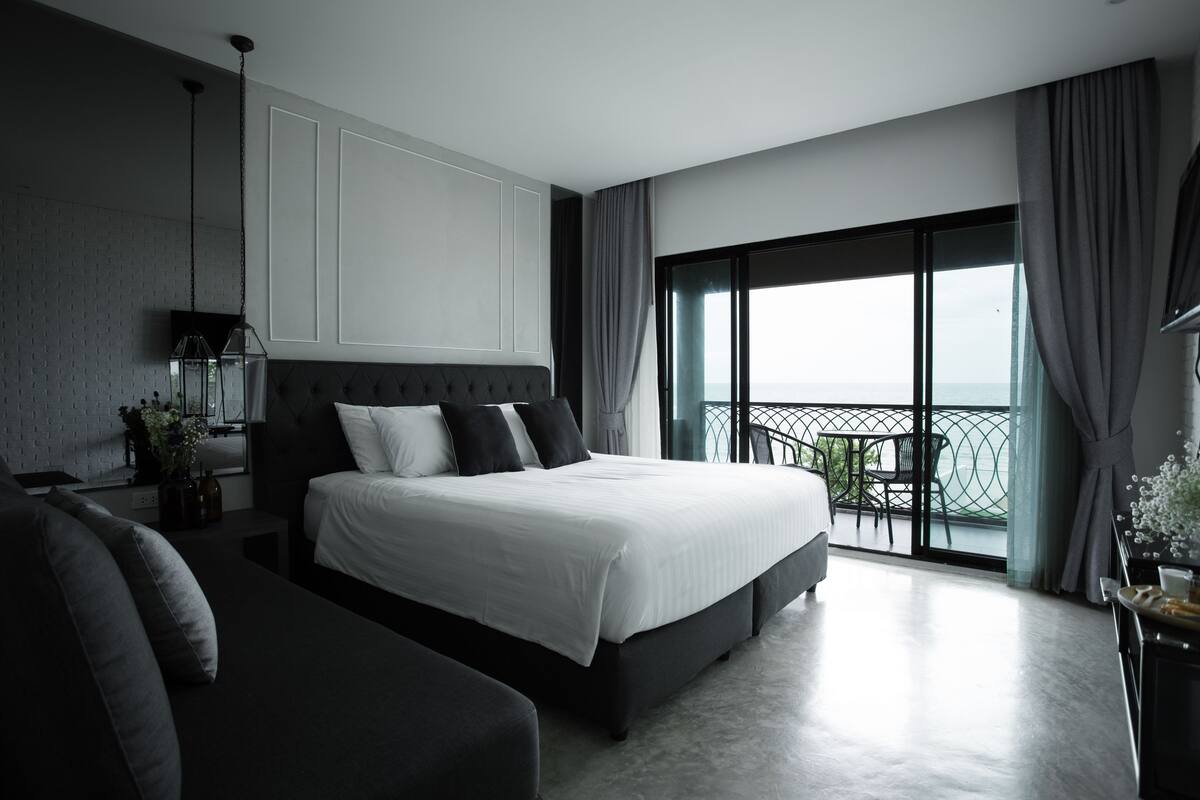 A modern hotel room with a large bed, a sofa, a balcony with a view, and a dining area.