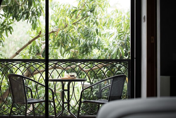 A balcony with two chairs and a small table, overlooking a lush green garden.