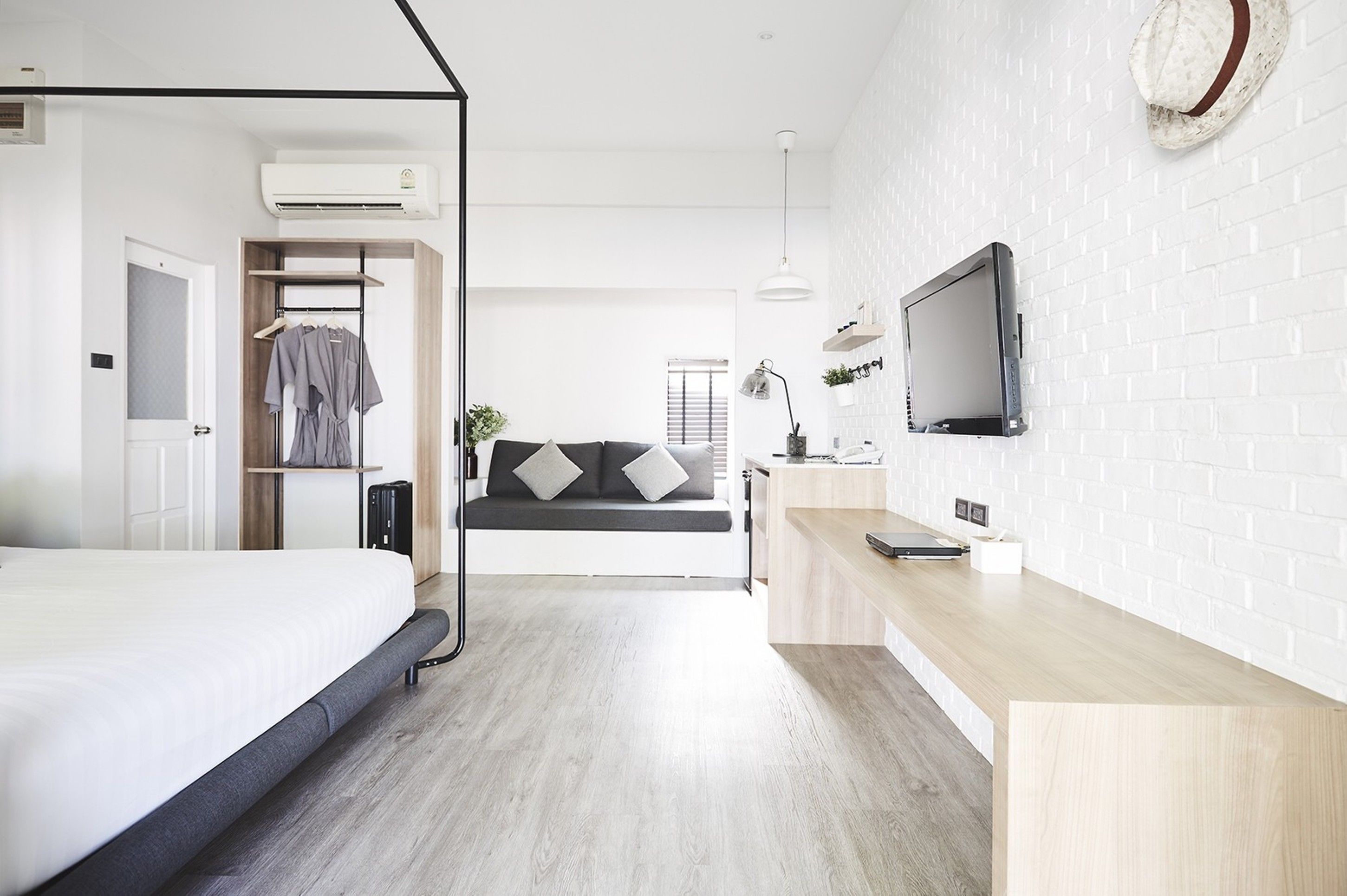 A modern hotel room with a bed, a seating area with a sofa, a TV mounted on the wall, and a wooden desk.